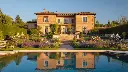 A luxurious house constructed from brick, perched elegantly on a hill, featuring a sparkling swimming pool and a vibrant garden bursting with colorful flowers, all perfectly reflected in a serene body of water or.webp